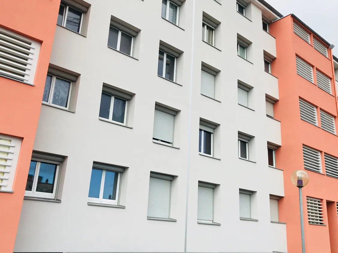 Façade d'une résidence de Miribel, blanche et orange, dont toutes les fenêtres sont équipées de volets roulants.